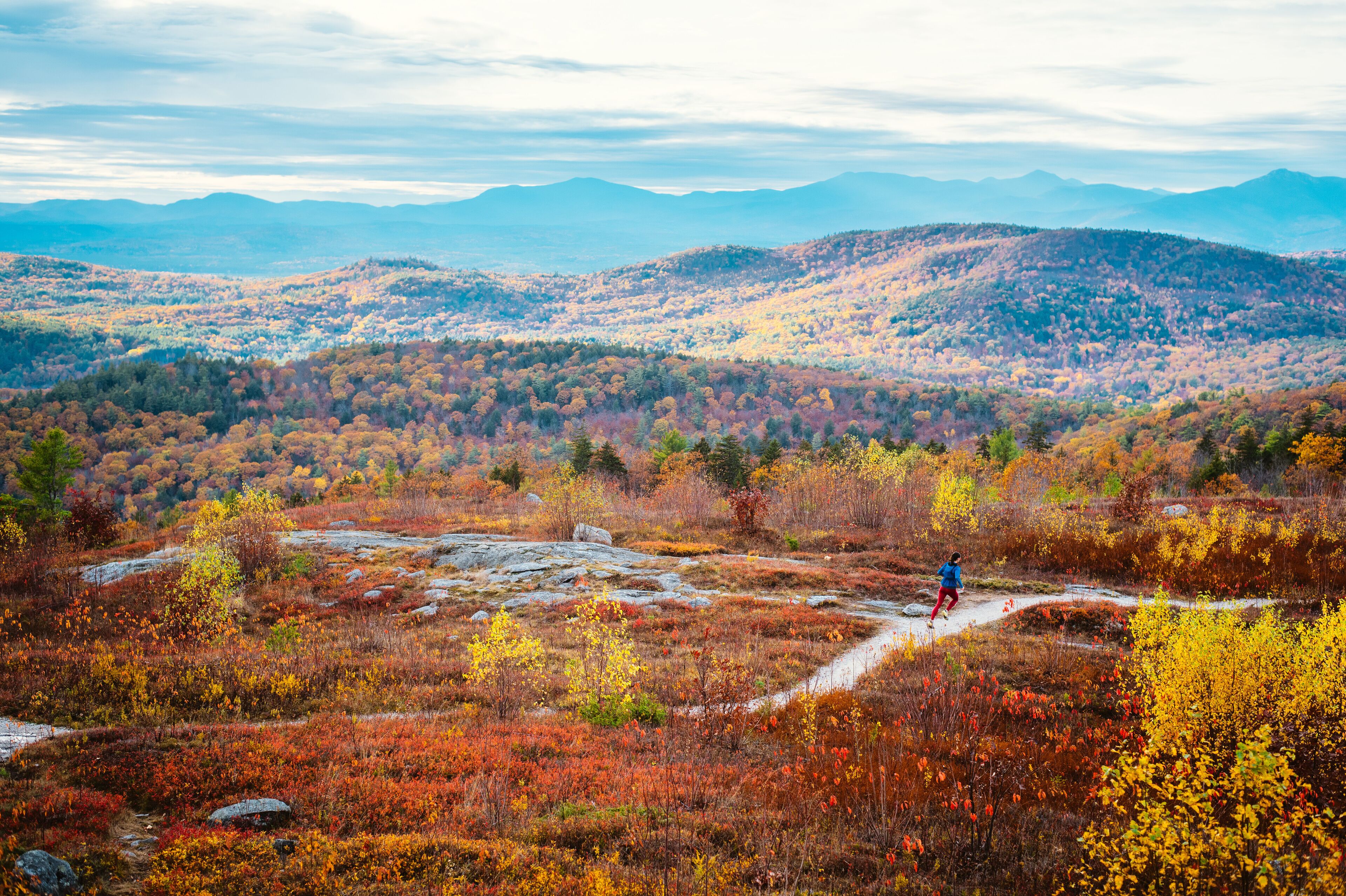 Woman trail running in mountains with foliage in autumn