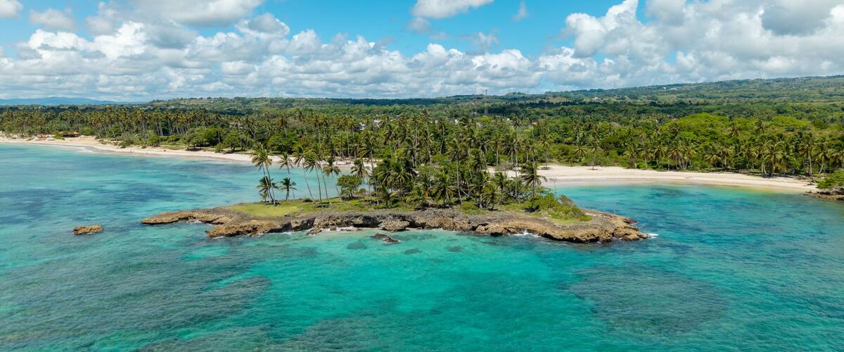 A tropical island surrounded by turquoise waters, palm trees, and a distant beach.