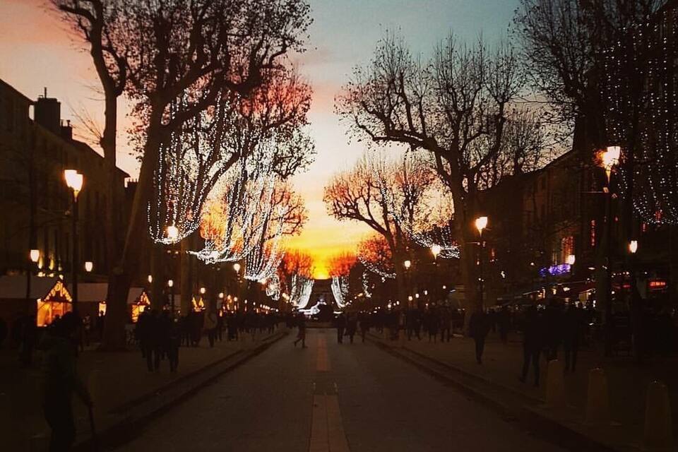 A tree-lined street at sunset with illuminated decorations.