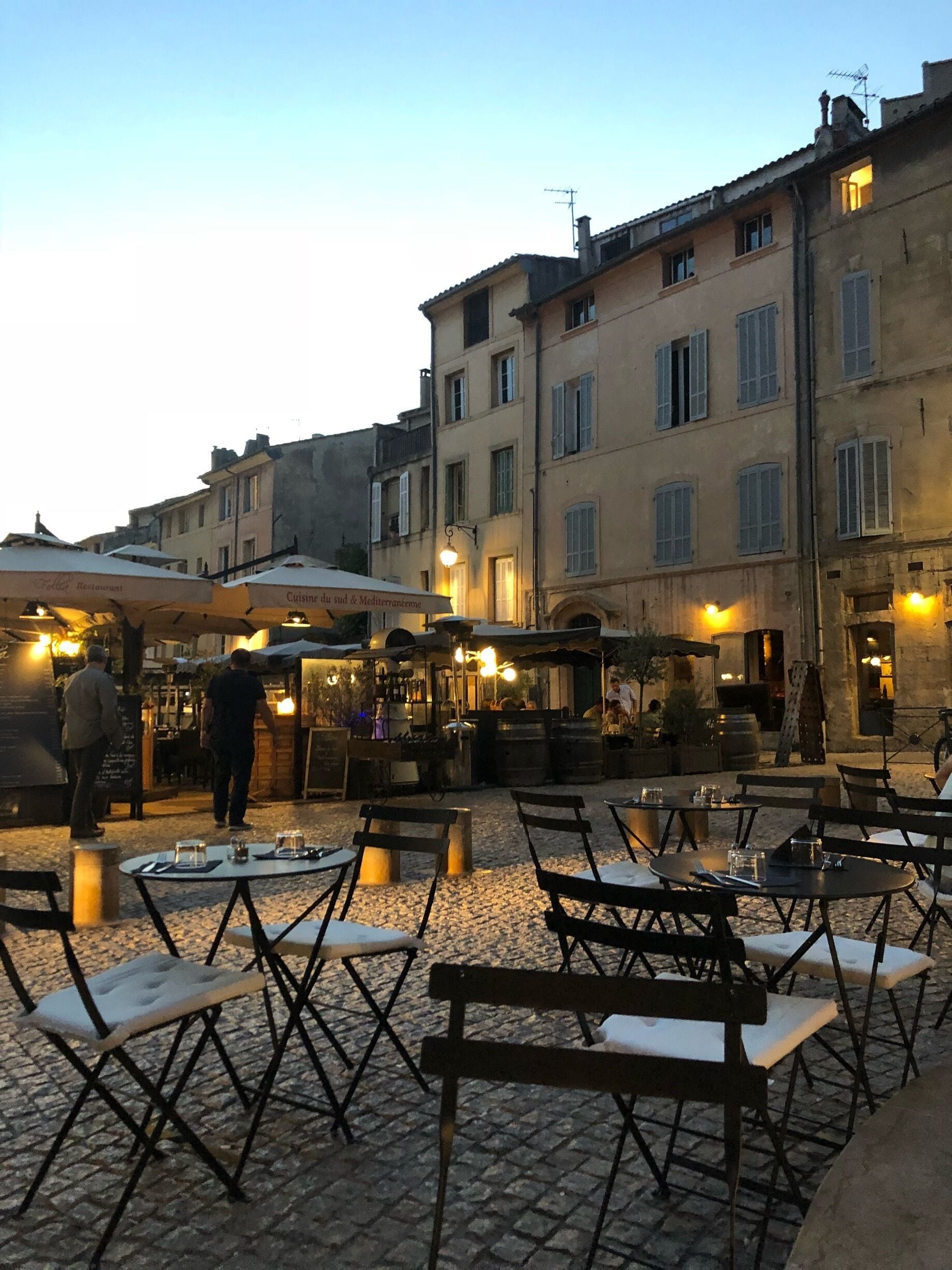 An outdoor café with tables and chairs, a street with buildings, and a person walking.