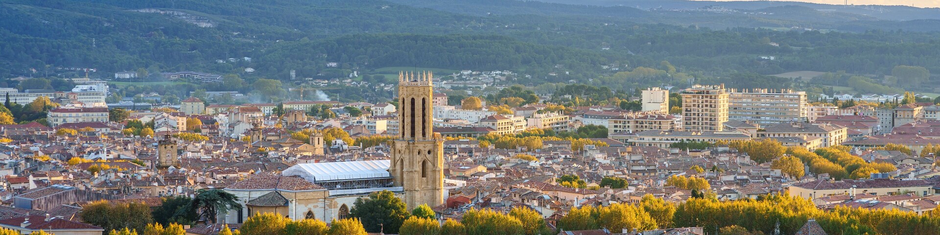 A cityscape with a prominent tower, surrounded by residential buildings and greenery, under a partly cloudy sky.