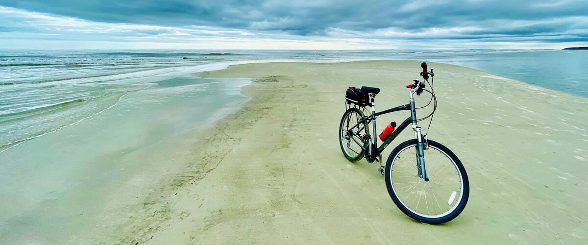 A bicycle on a sandy beach with the ocean in the background.
