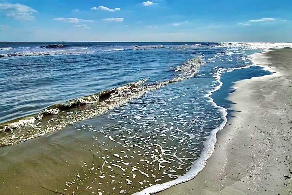 Una playa arenosa con olas suaves acariciando la orilla bajo un cielo azul despejado.