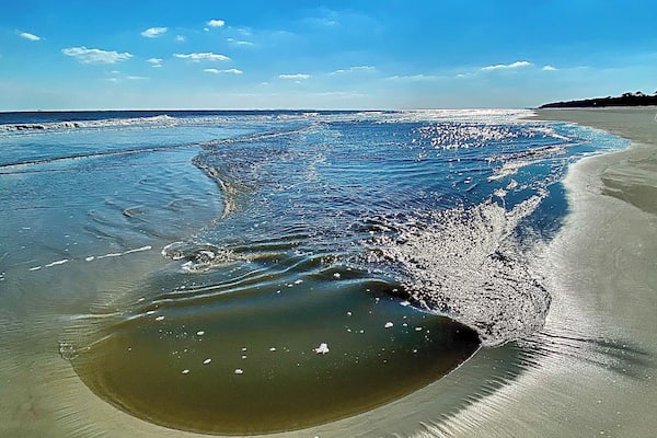 A beach with clear blue water, a sandy shore, and a distant shoreline.