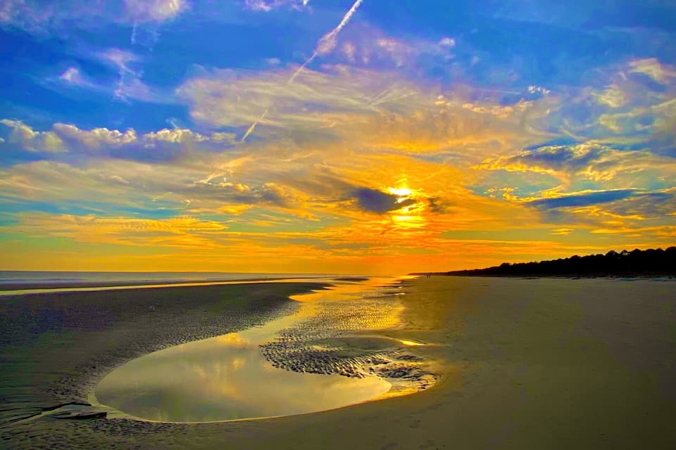 A beach with a sunset, clouds, and a reflection in the water.