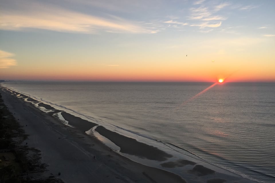 A beach at sunset with a clear sky and calm sea.