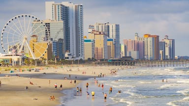 A beach with people, a large Ferris wheel, and tall buildings in the background.