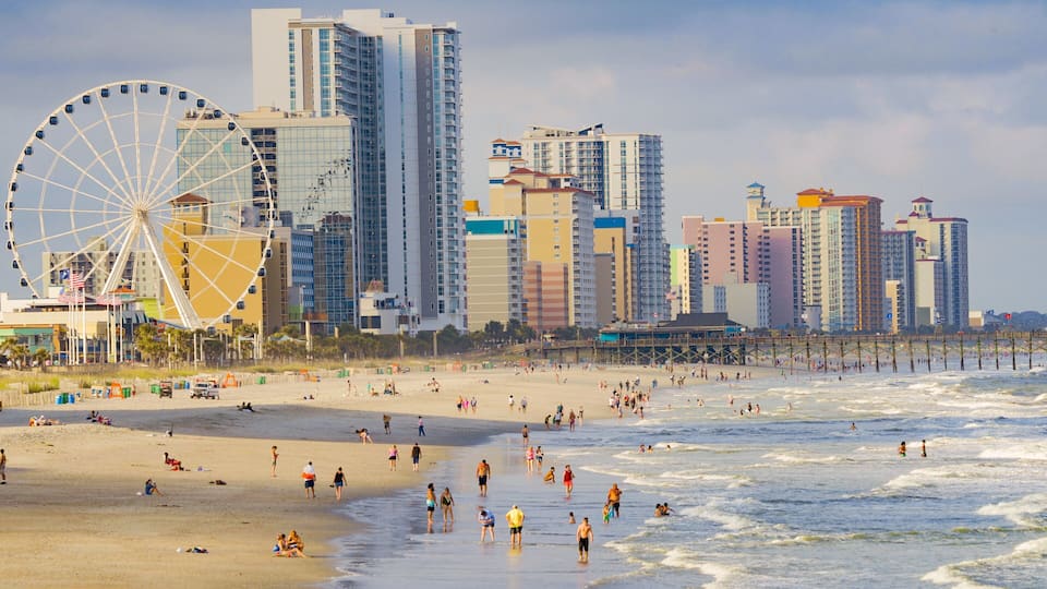 A beach with people, a large Ferris wheel, and tall buildings in the background.