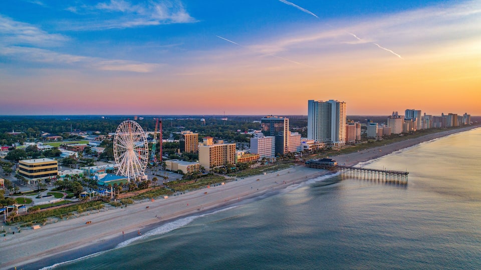 A coastal cityscape with a prominent Ferris wheel, beachfront, and high-rise buildings.