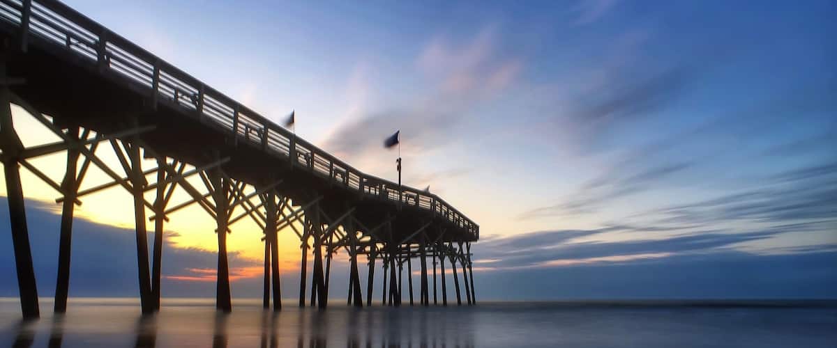 A pier extending into calm waters at sunset with a clear sky.