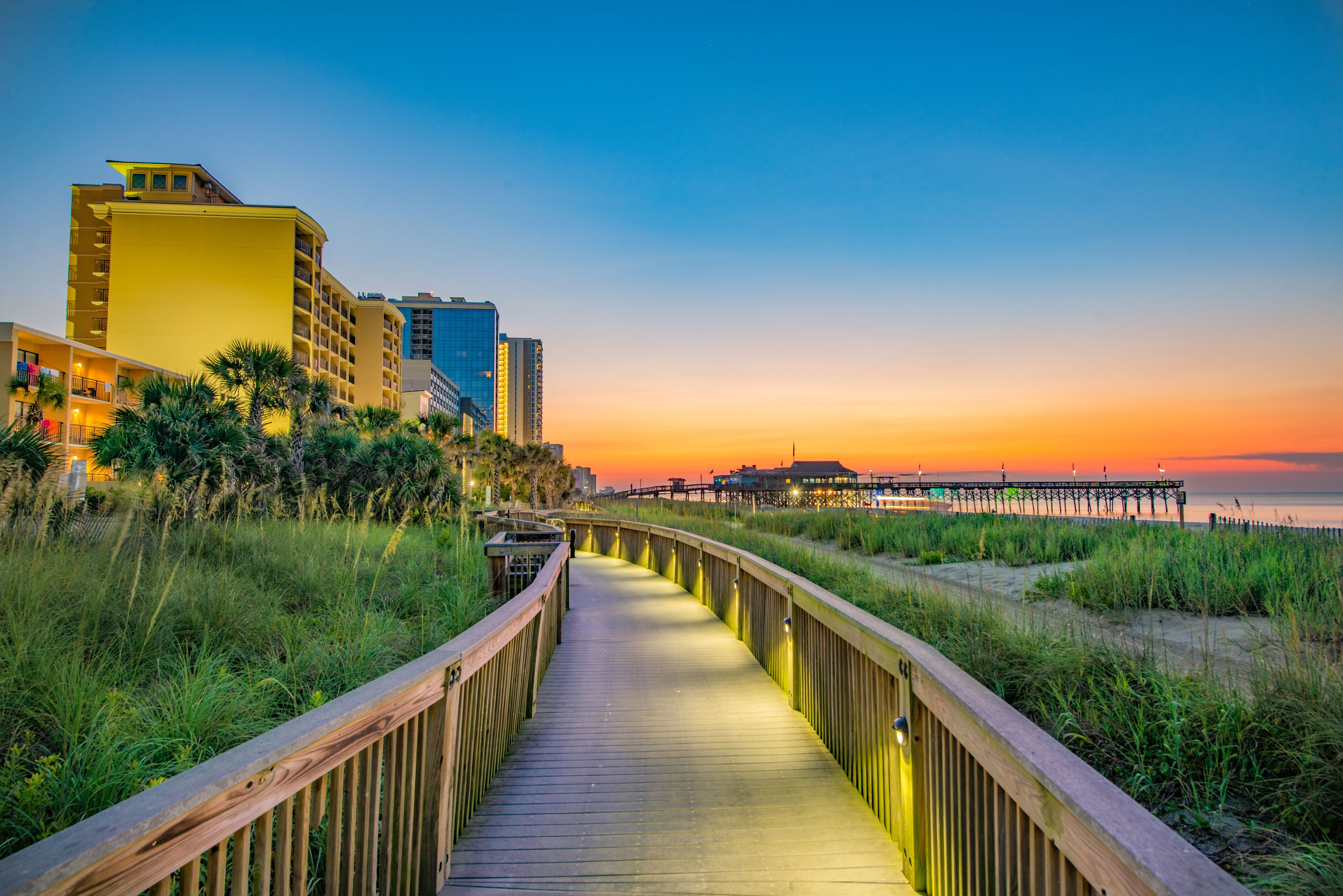 A wooden boardwalk leading to a pier with buildings in the background.