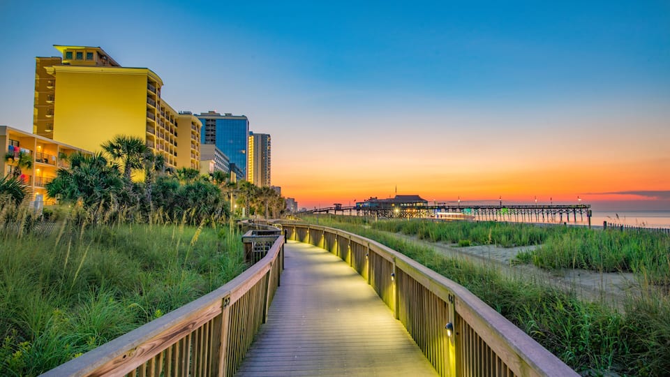 A wooden boardwalk leading to a pier with buildings in the background.