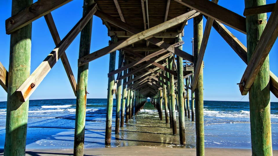 A wooden pier extending into the ocean with clear blue skies.