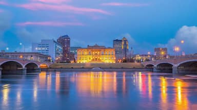 A cityscape with a river, a bridge, and illuminated buildings at dusk.
