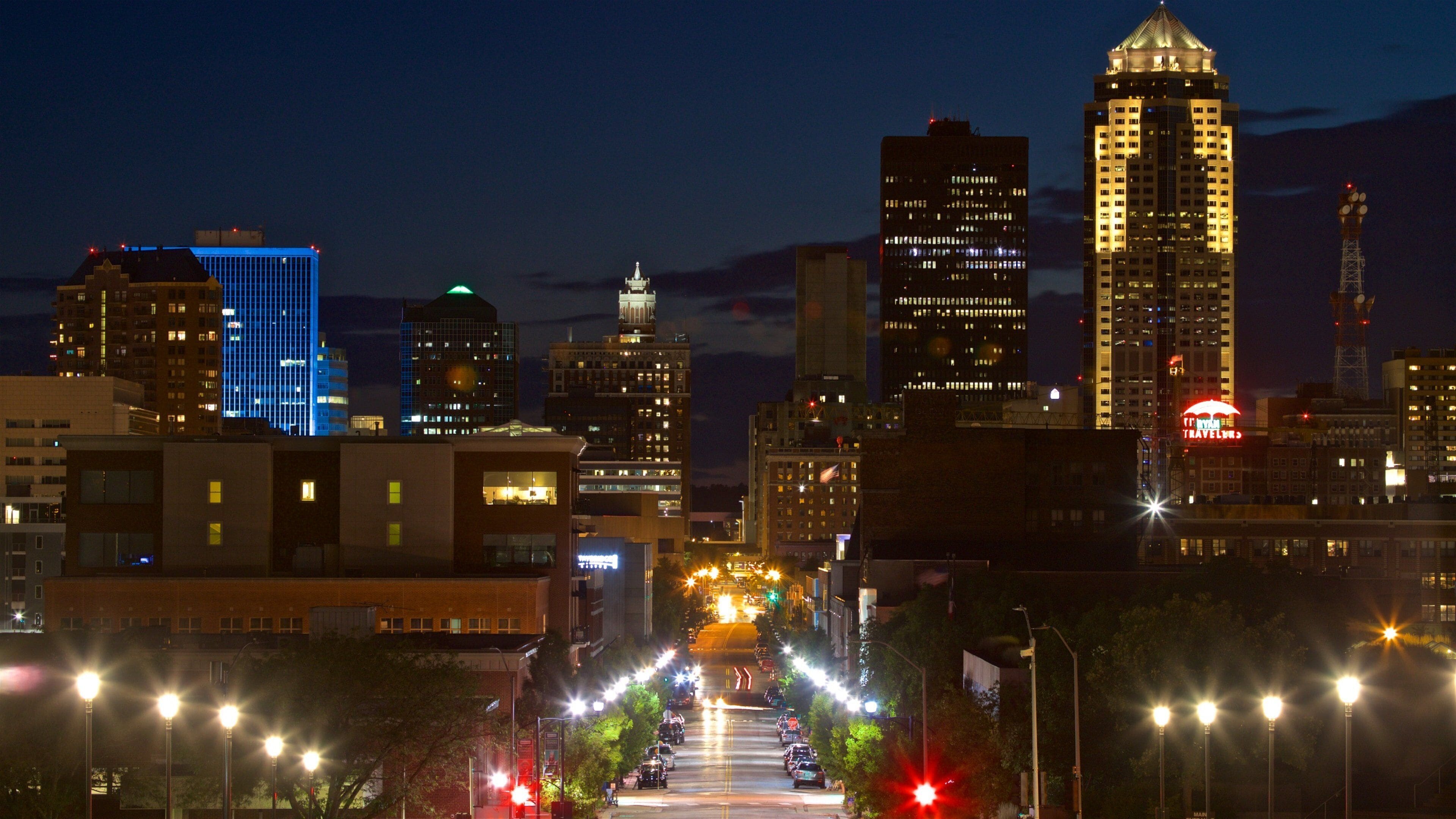 A city skyline at night with illuminated buildings and a street with streetlights.