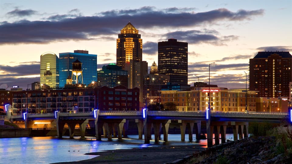 A city skyline at dusk with illuminated buildings and a bridge over a river.