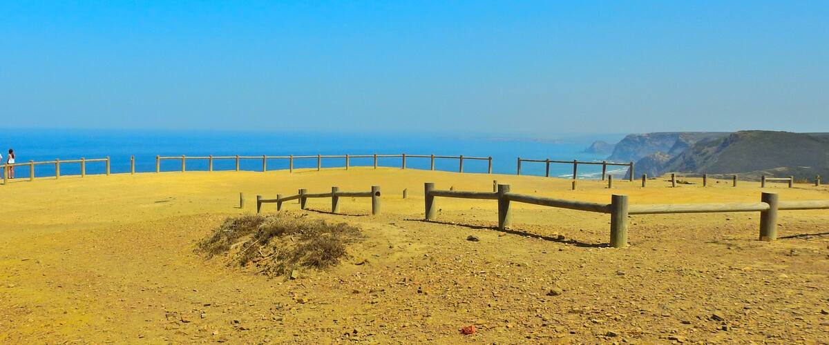 A coastal landscape with a sandy area, wooden fences, and a clear view of the ocean.