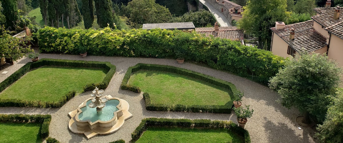 A lush garden with a fountain, terraced houses, and a winding path.
