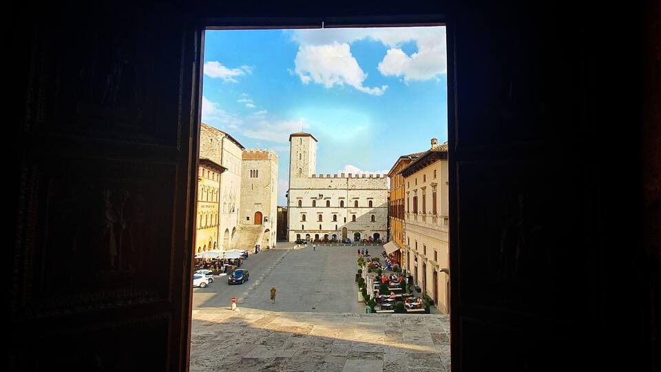 A view of a historic square with a prominent building with a tower, surrounded by traditional architecture.