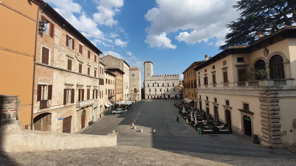 A historic square with stone buildings, a tower, and outdoor seating areas.
