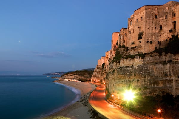 Una strada costiera con un edificio a picco sulla scogliera e una spiaggia.