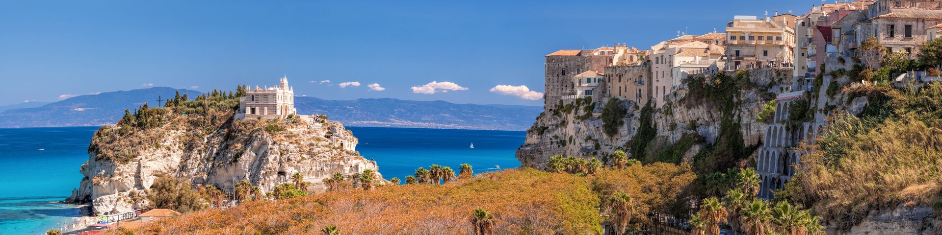 Un pueblo costero con edificios históricos, una iglesia destacada en un acantilado y un mar azul cristalino.
