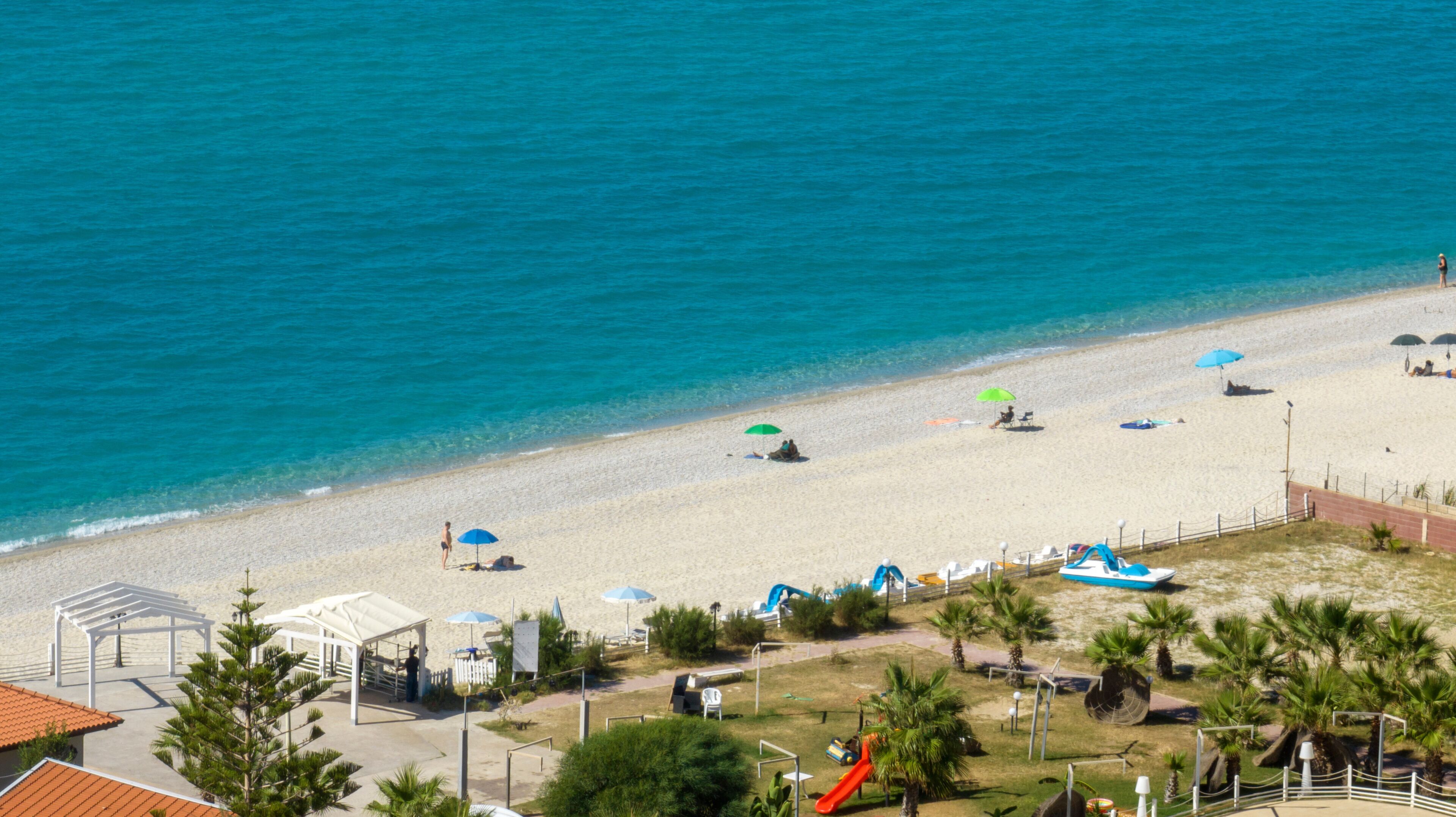 A beach with clear blue water, umbrellas, and a playground.