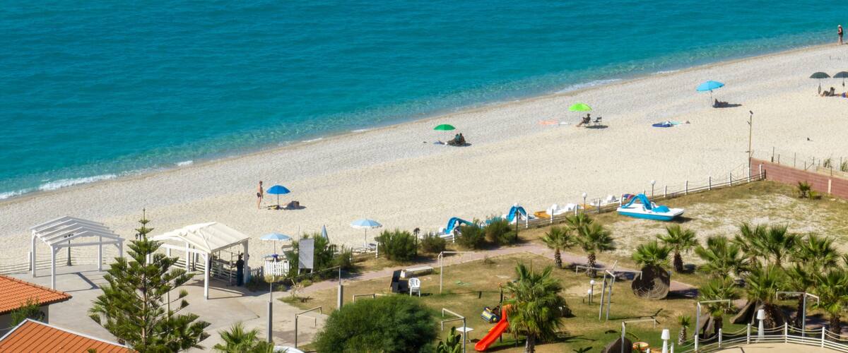 A beach with clear blue water, umbrellas, and a playground.