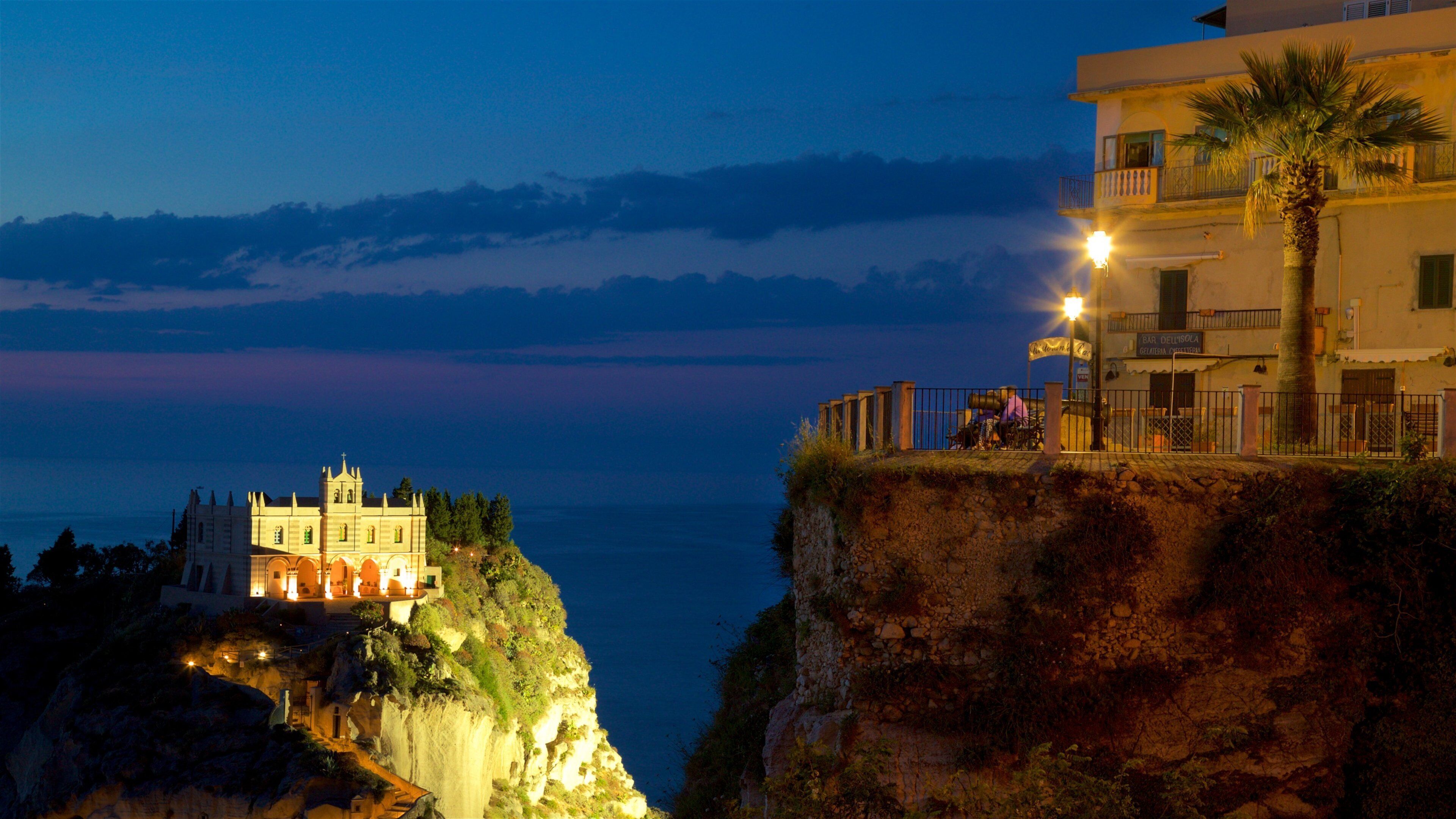 A coastal cliff with a historic building and a modern building with a palm tree.