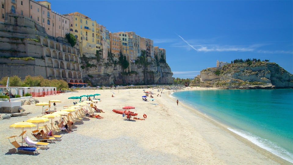 A beach with clear turquoise water, a sandy shore, and buildings on the cliffside.