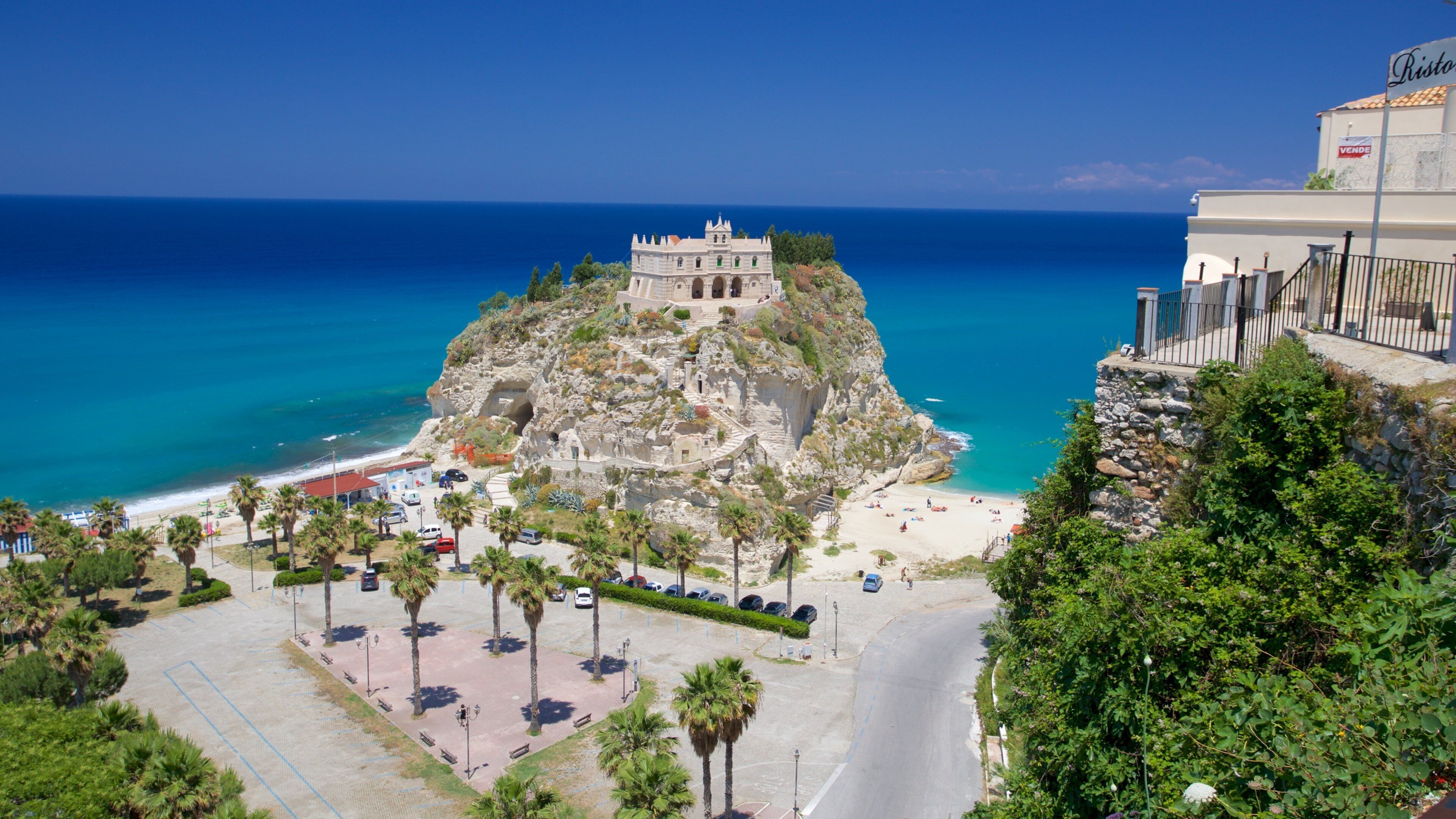 A coastal town with a historic castle on a rocky hill, a beach, and a modern building labeled "Risto".
