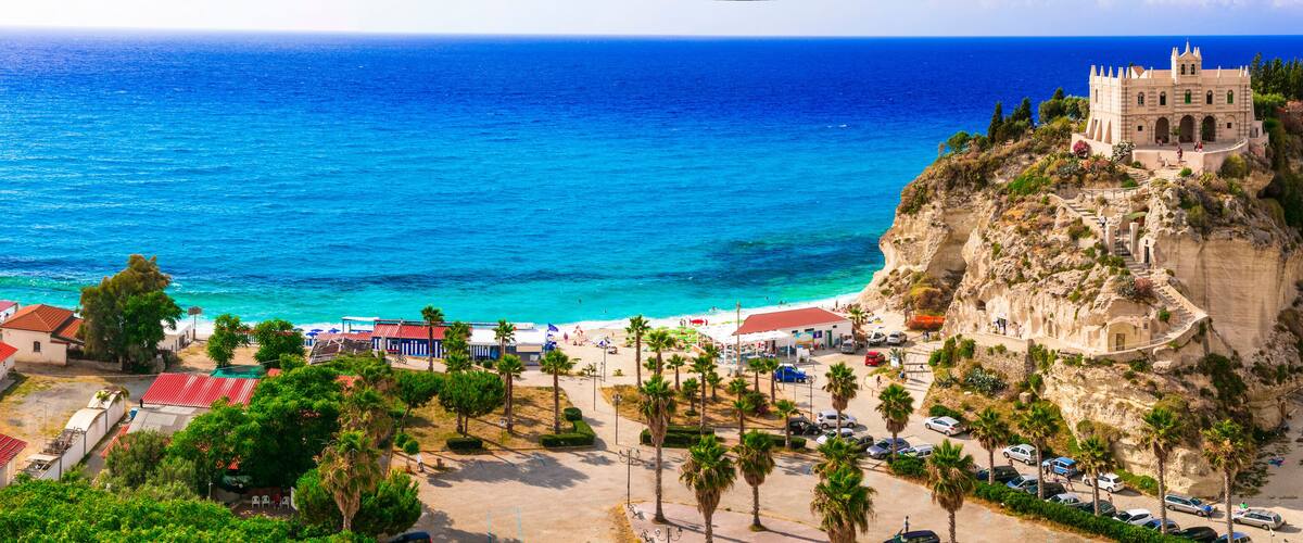 A coastal town with a prominent castle on a cliff, a beach, and a clear blue sea.