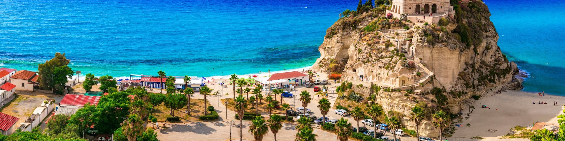 A coastal town with a prominent castle on a cliff, a beach, and a clear blue sea.