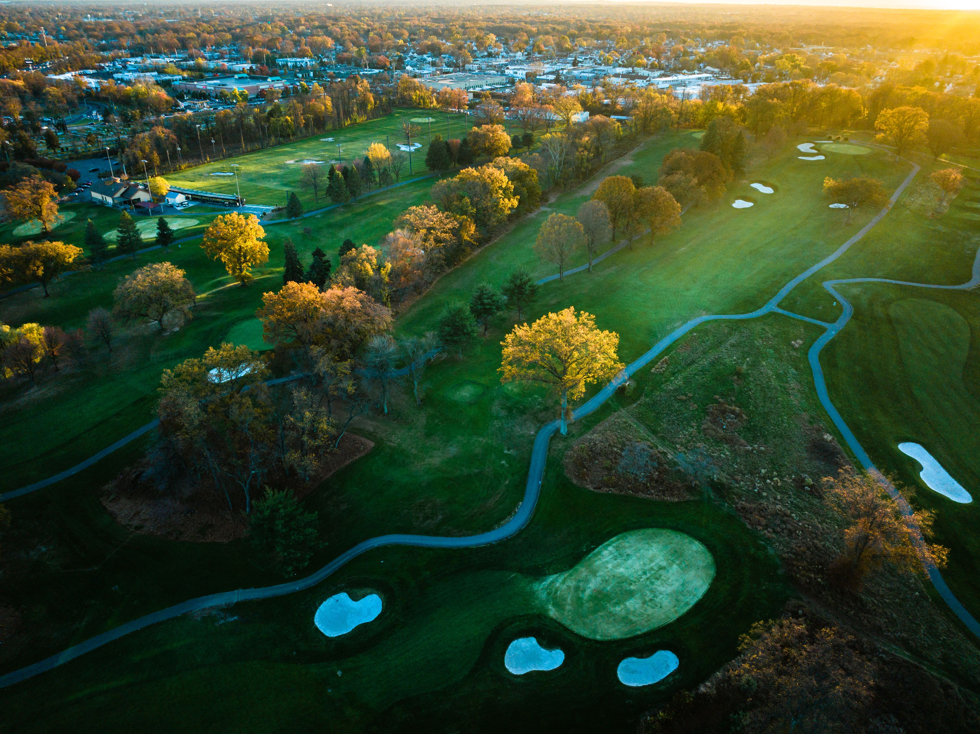 Vue aérienne d’un terrain de golf avec de nombreux bunkers et un quartier résidentiel environnant.
