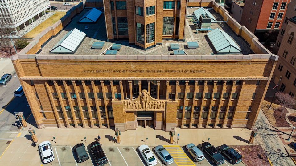A large brick building with a central entrance and a row of parked cars in front.