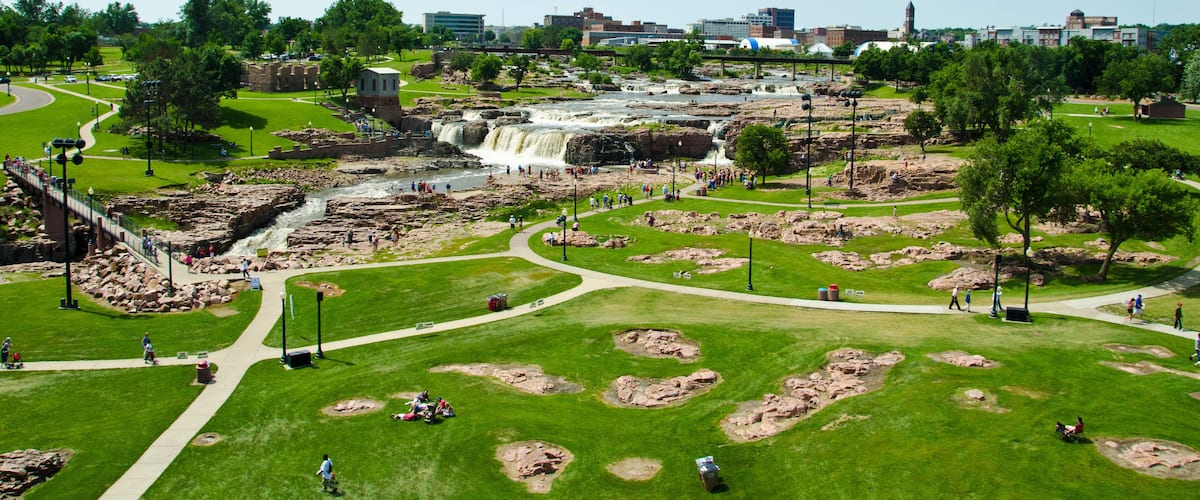 A park with a waterfall, walking paths, and a bridge.