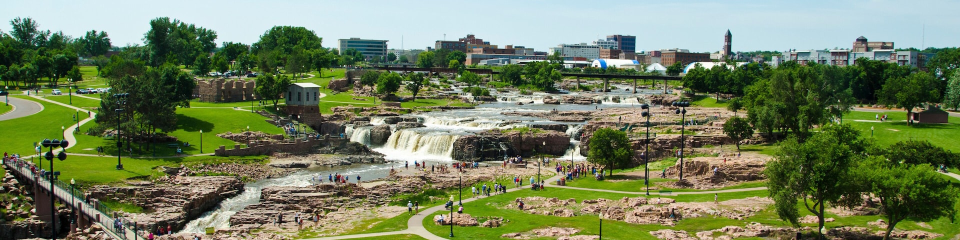 A park with a waterfall, walking paths, and a bridge.