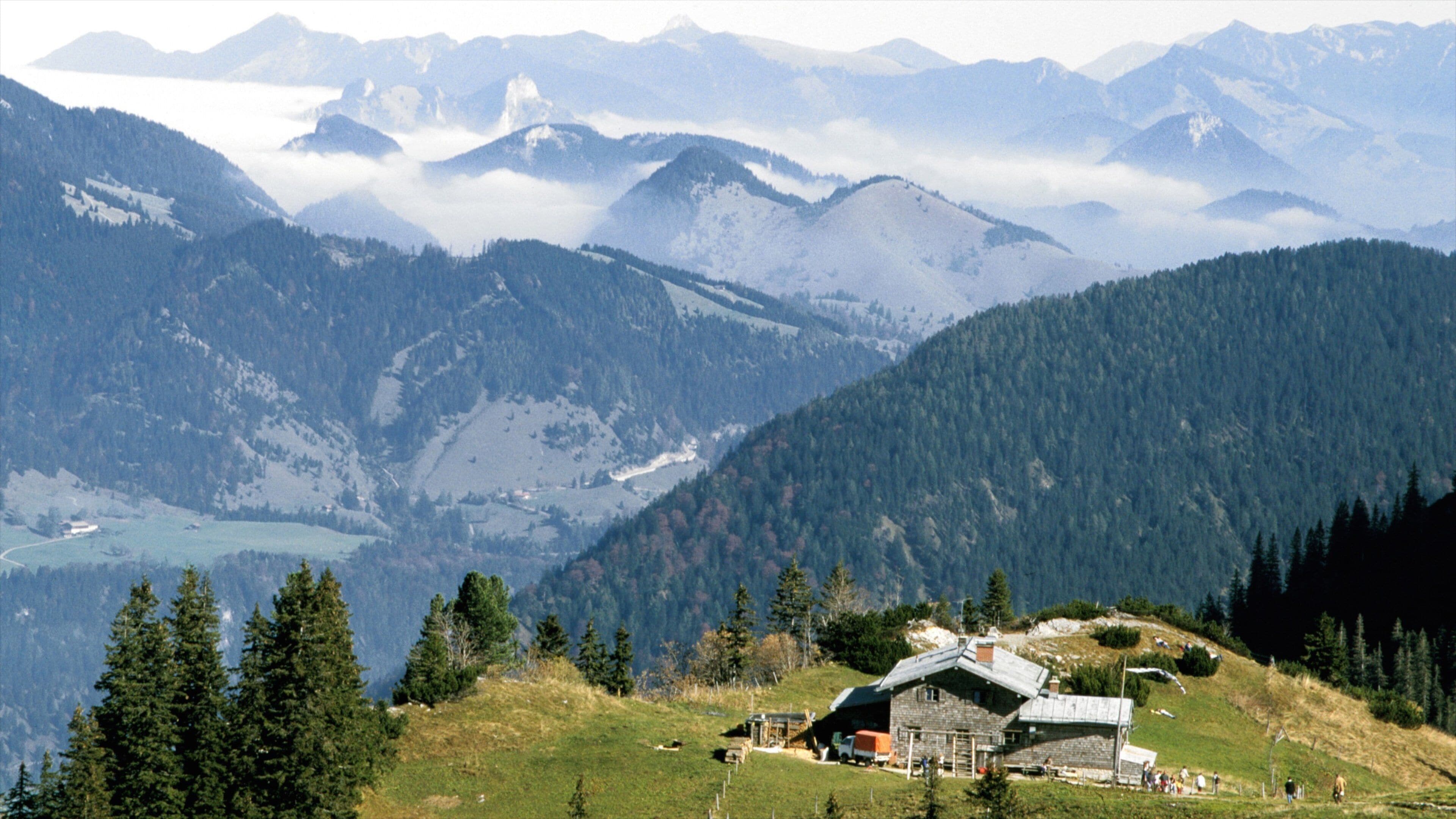 A mountain landscape with a cabin and forested hills.