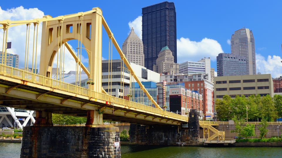 A yellow bridge over a river with a city skyline in the background.