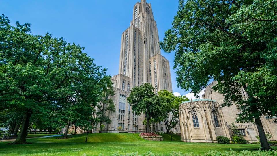 A historic building with a tall tower, surrounded by lush green trees and a well-maintained lawn.