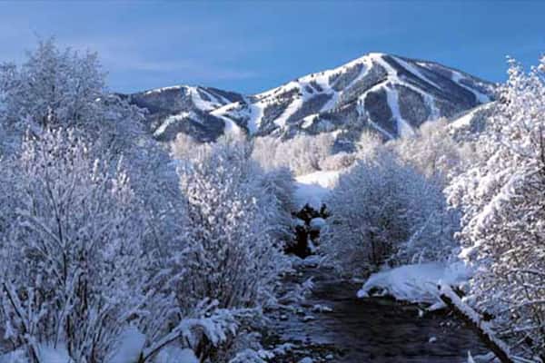 A snow-covered landscape with a river, trees, and mountains.