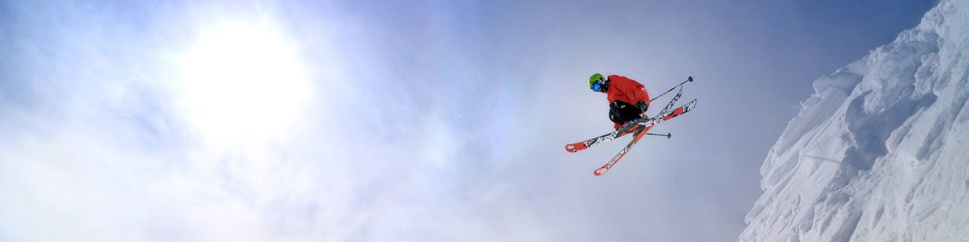 A skier in mid-air against a clear sky and snow-covered mountain.