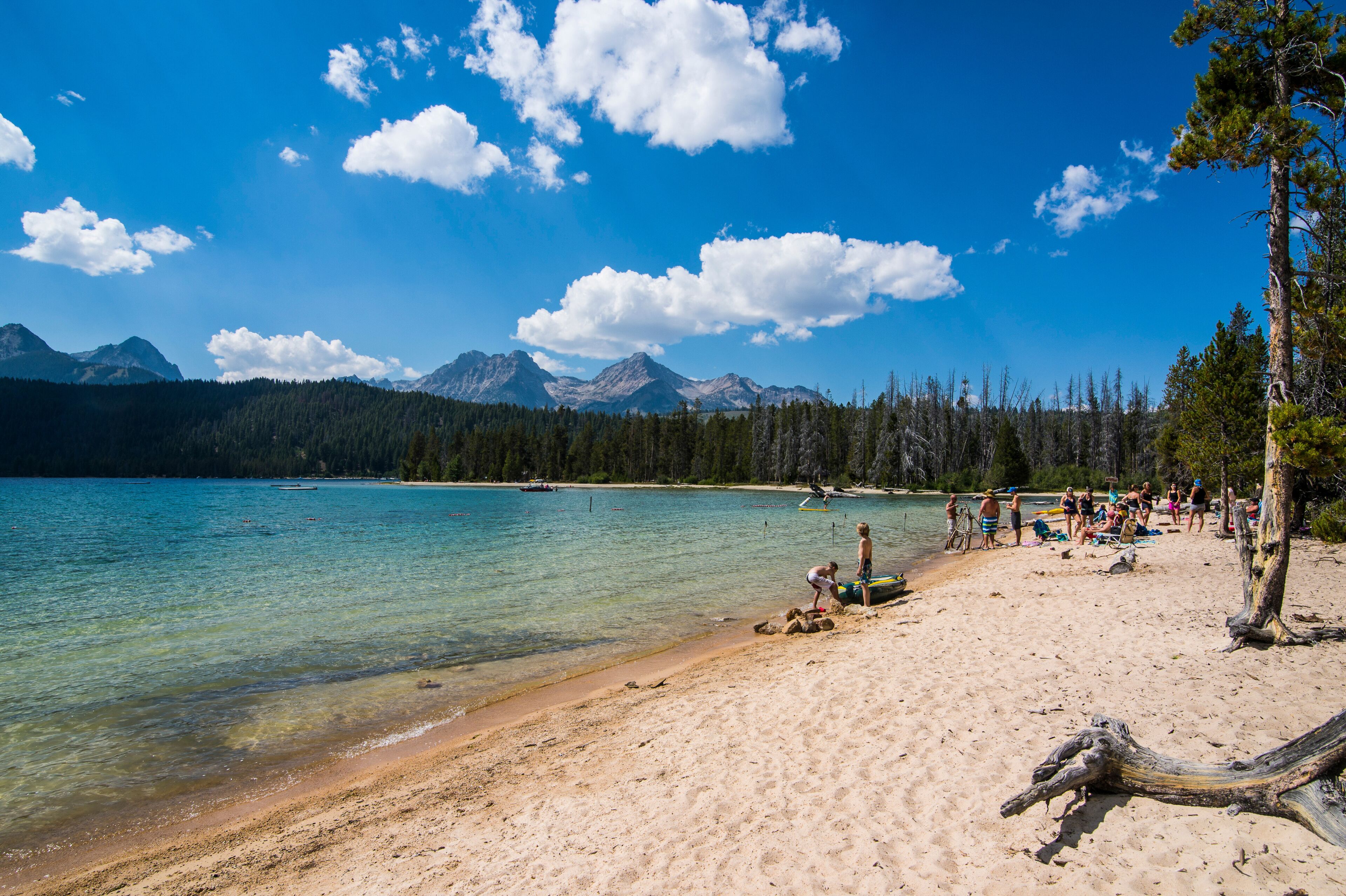 A beach with clear turquoise water, a sandy shore, and a backdrop of mountains and trees.