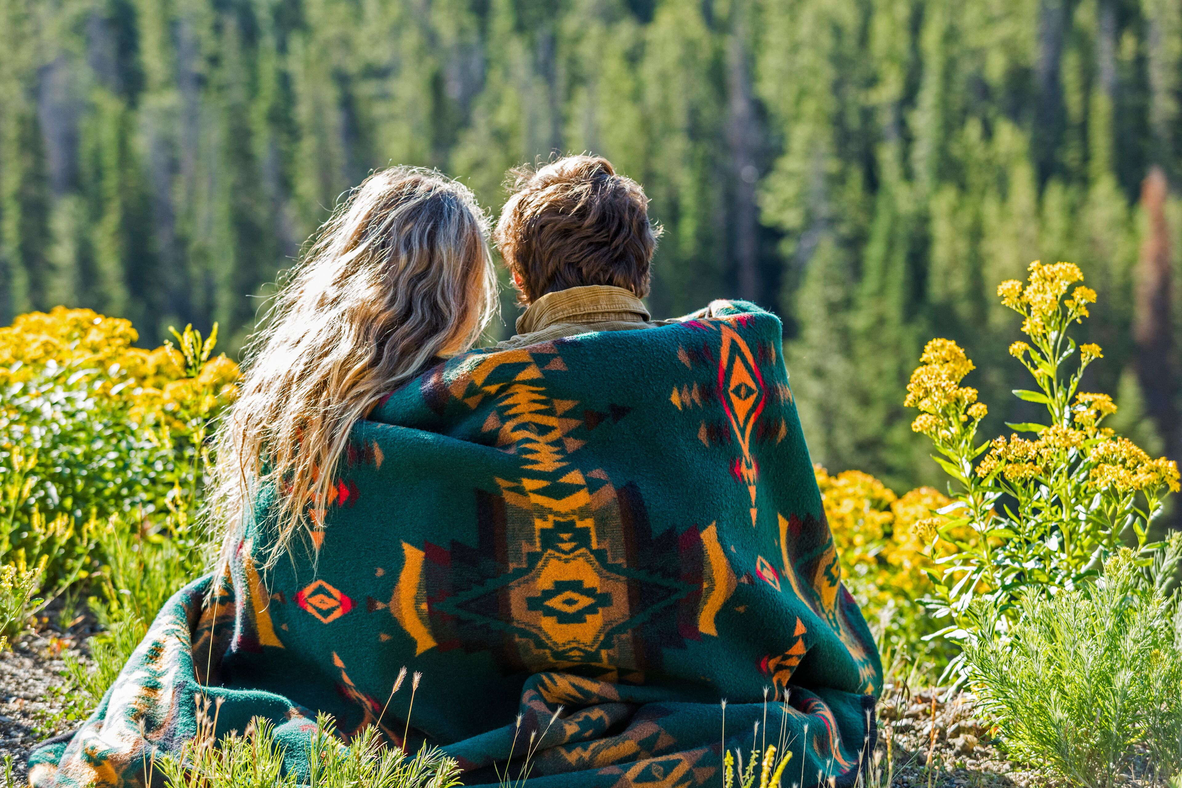 Una pareja sentada en un campo con un bosque al fondo.