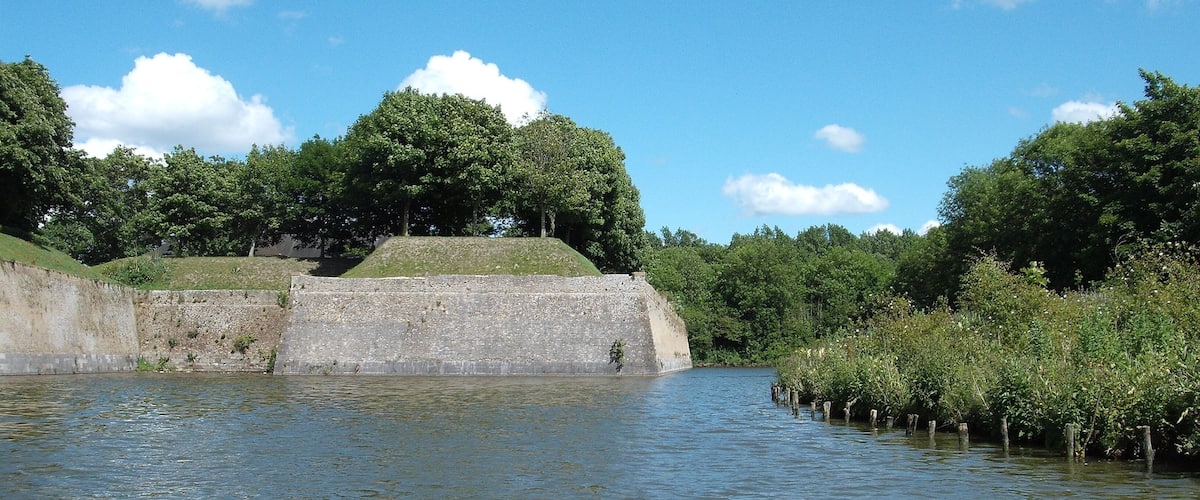 A calm river with a stone embankment and trees in the background.