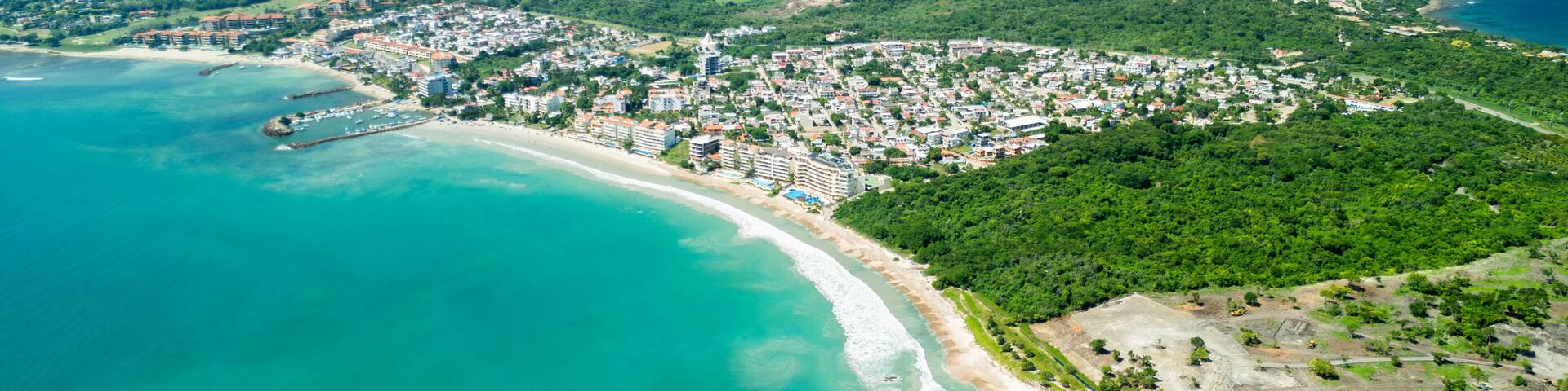 A coastal town with a beach, dense residential area, and a forested hill.