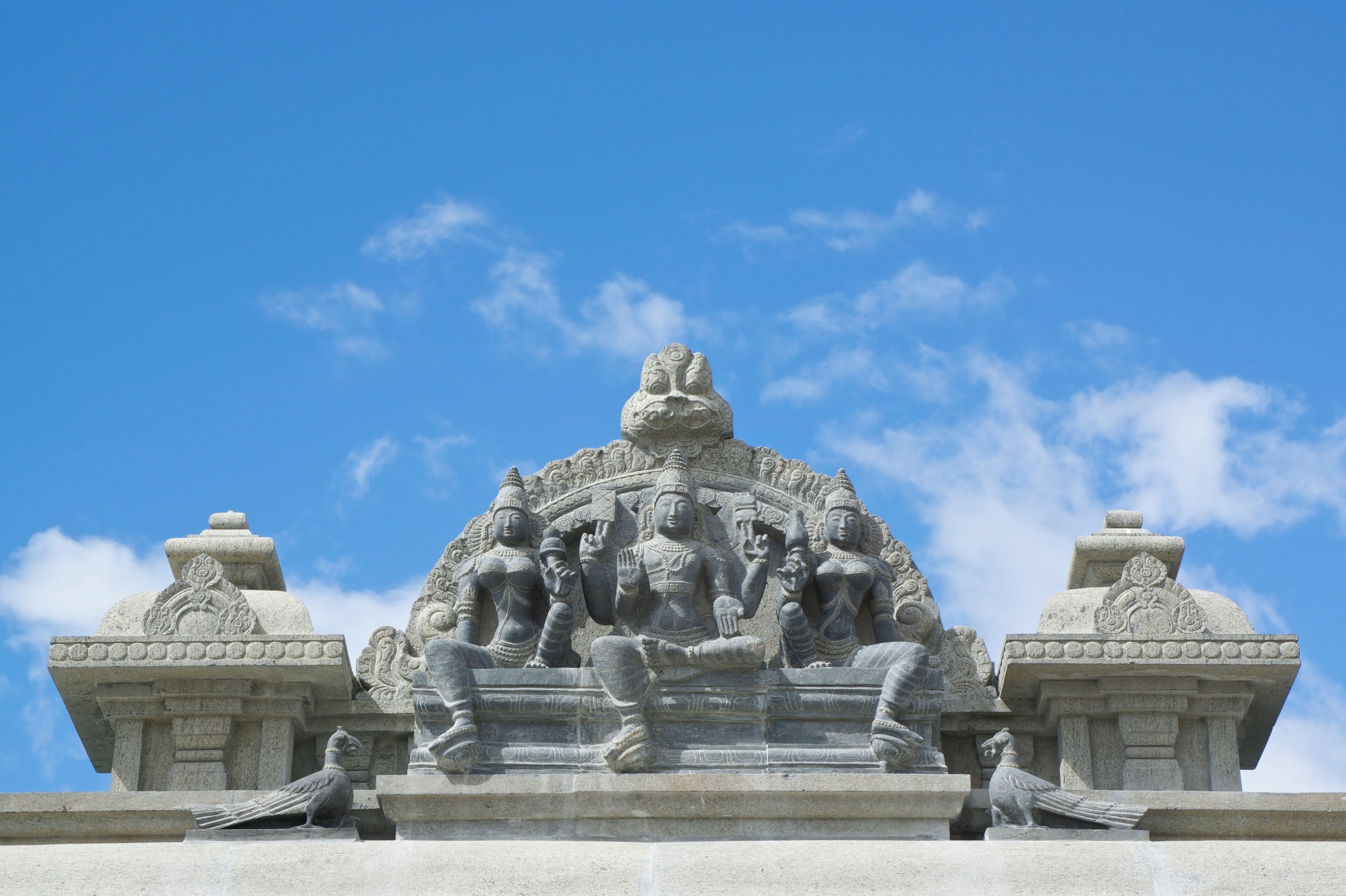 A stone sculpture of multiple figures with intricate carvings, set against a clear blue sky.