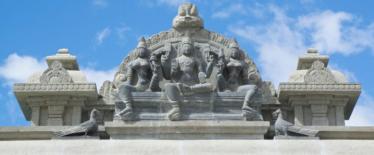 A stone sculpture of multiple figures with intricate carvings, set against a clear blue sky.