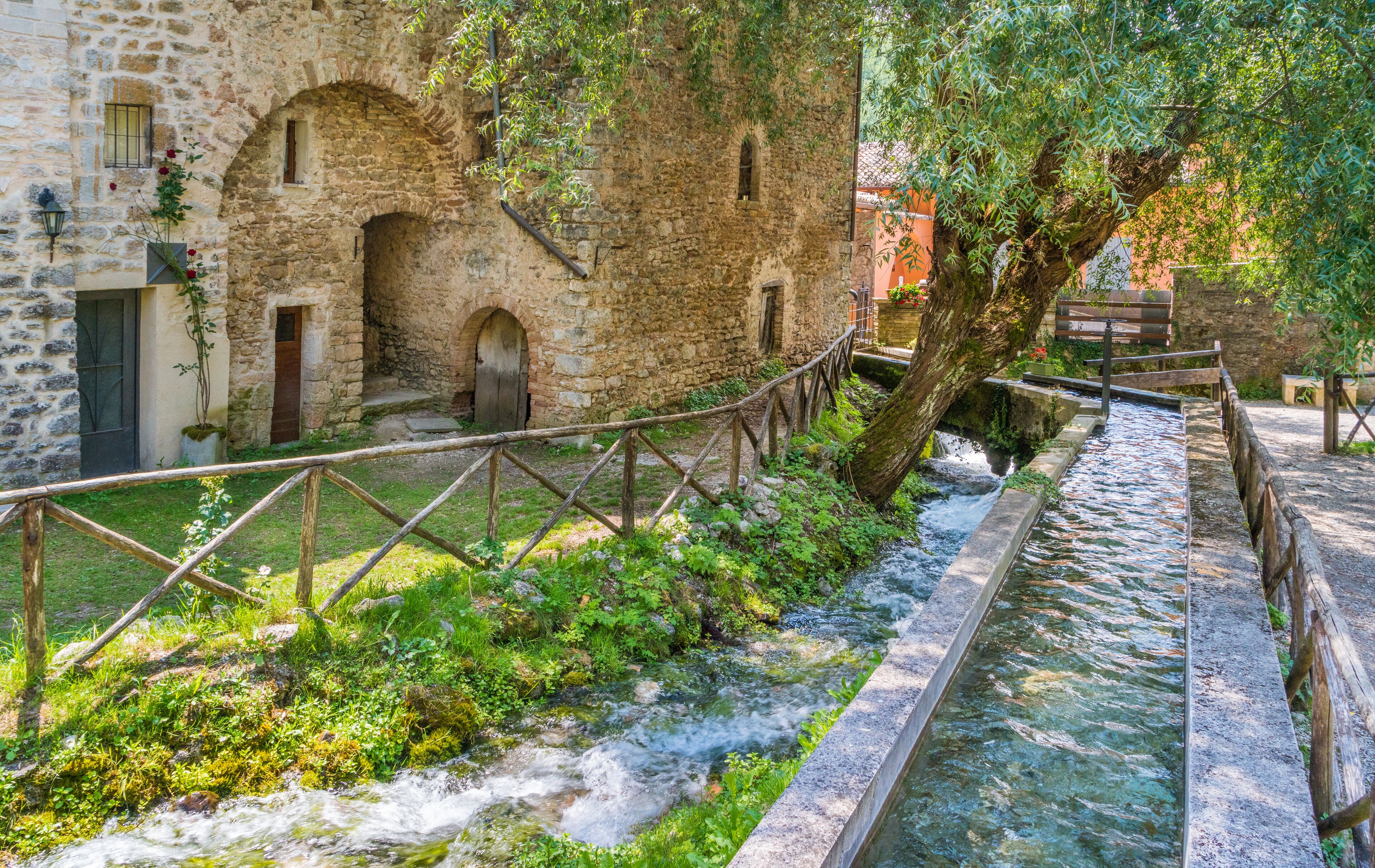Un edificio de piedra con ventanas arqueadas y un puente de madera sobre un arroyo.
