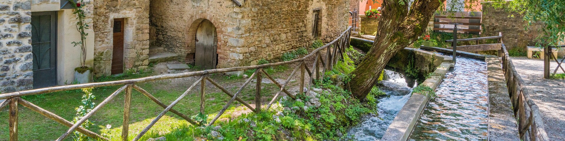 Un edificio de piedra con ventanas arqueadas y un puente de madera sobre un arroyo.